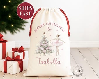 May include: Cream-colored Christmas gift bag with red drawstring closure. The bag features a watercolor illustration of a Christmas tree, a ballerina, and the text "Merry Christmas to Isabella".