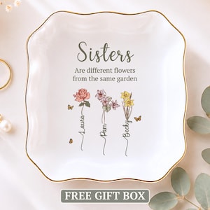 May include: A white square ceramic trinket dish with gold trim featuring the text Sisters Are different flowers from the same garden, with illustrations of three flowers labeled Laura, Pam, and Becky, accompanied by small butterfly graphics.