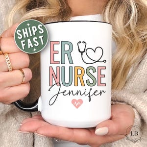 Puede incluir: Taza de cer&aacute;mica blanca con interior y asa negros. La taza presenta el texto "ER NURSE Jennifer" en letras de colores y un dise&ntilde;o de estetoscopio. Tambi&eacute;n hay un coraz&oacute;n con un gr&aacute;fico de latido card&iacute;aco.