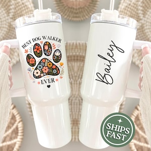 May include: Two white insulated tumblers with handles. One features a floral paw print design with the text "Best Dog Walker Ever." The other has the name "Bailey" in script. Both have clear lids and straws.