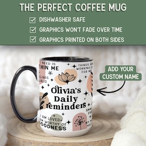 May include: A white ceramic coffee mug with a black handle and rim. The mug features the text "Olivia's Daily reminders" with floral and abstract designs in black, peach, and green. The mug is dishwasher safe and has graphics printed on both sides.