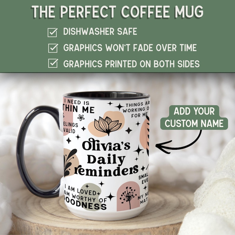 May include: A white ceramic coffee mug with a black handle and rim. The mug features the text "Olivia's Daily reminders" with floral and abstract designs in black, peach, and green. The mug is dishwasher safe and has graphics printed on both sides.