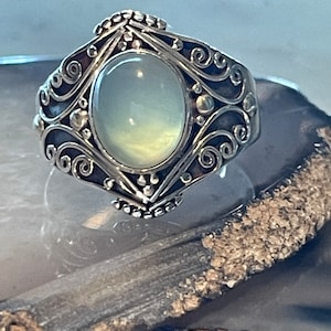 May include: A silver ring with an oval-shaped, milky white gemstone set in a filigree design.
