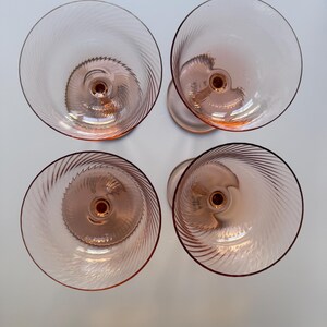 May include: Overhead view of four pink-tinted glass goblets. Each goblet features a spiral design in the bowl and a stem. The glasses are arranged in a square formation, showcasing their elegant design and color.