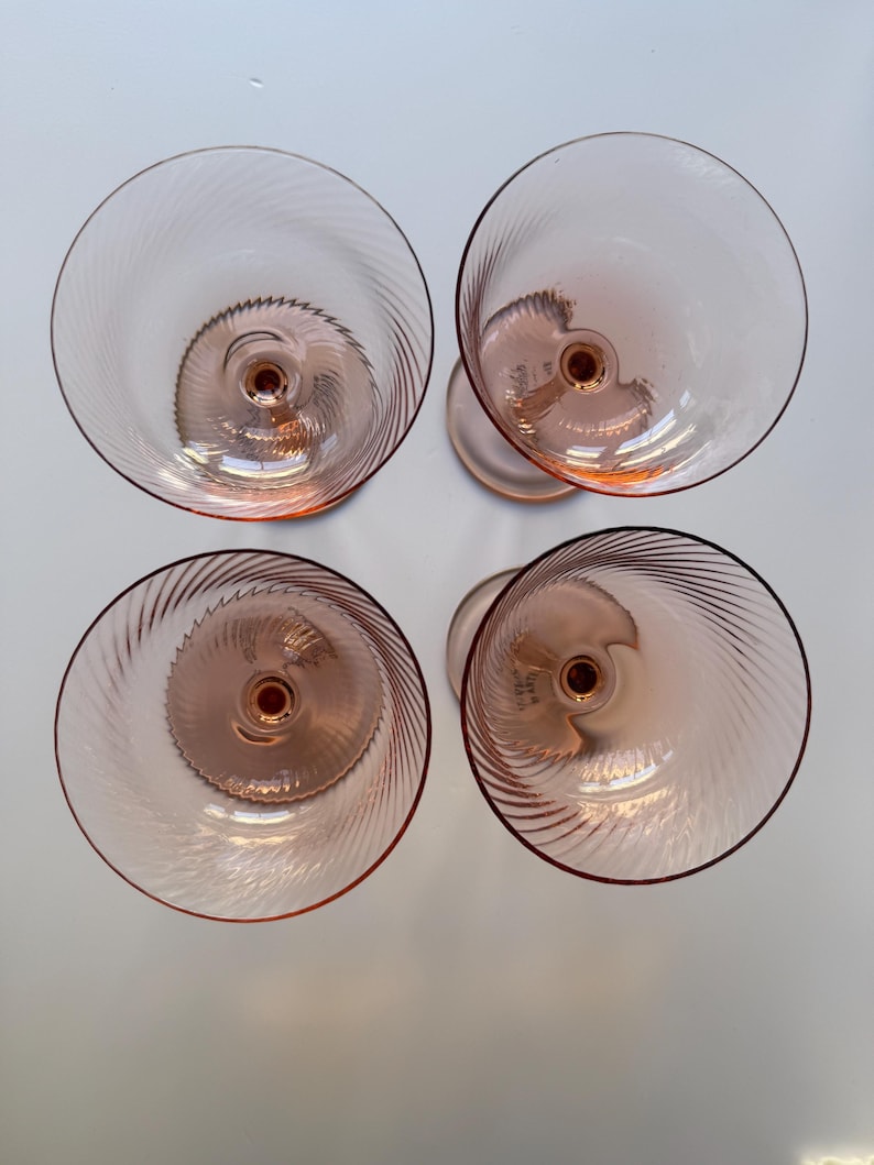 May include: Overhead view of four pink-tinted glass goblets. Each goblet features a spiral design in the bowl and a stem. The glasses are arranged in a square formation, showcasing their elegant design and color.