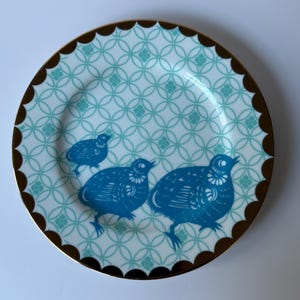 May include: A decorative plate with a teal and white geometric pattern and a scalloped brown rim. Three blue bird illustrations are featured on the plate. The plate is a stylish addition to any home decor.
