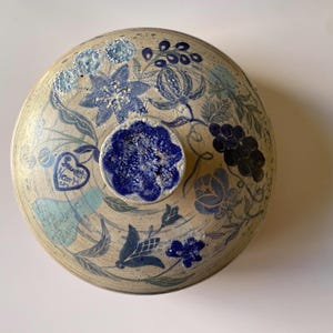 Puede incluir: Un tazón de cerámica con tapa, fondo blanco y diseños florales azules. La tapa tiene un diseño floral azul en el centro.