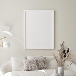 May include: A contemporary living room featuring a white sofa, two patterned cushions, and a circular coffee table. A blank white picture frame is mounted on the wall above the sofa. A gold floor lamp and a vase with dried plants complete the decor.