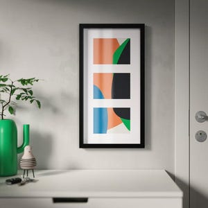 Peut inclure: Une impression d'art encadrée avec un cadre noir. L'œuvre présente trois sections rectangulaires avec des formes abstraites en orange, noir, vert et bleu sur fond blanc. L'impression est accrochée à un mur gris.
