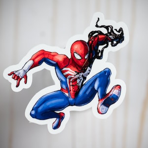 May include: A red and blue superhero sticker with black webbing and a black and white face. The superhero is jumping and has a black and white symbol on their chest.