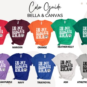K&ouml;nnte beinhalten: Farbguide f&uuml;r Bella + Canvas T-Shirts in verschiedenen Farben, darunter Rot, Maroon, Orange, Heather Kelly, Kelly, Heather Team Purple, Navy, True Royal, Ash und Athletic Heather. Jedes Shirt zeigt den Text "IN MY BOBCATS ERA" mit einem Pfotenabdruck.
