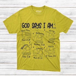 Puede incluir: Camiseta amarillo mostaza con un dise&ntilde;o gr&aacute;fico negro que presenta veh&iacute;culos de construcci&oacute;n y el texto "GOD SAYS I AM..." con varias afirmaciones y vers&iacute;culos b&iacute;blicos. La camiseta es de un material suave.