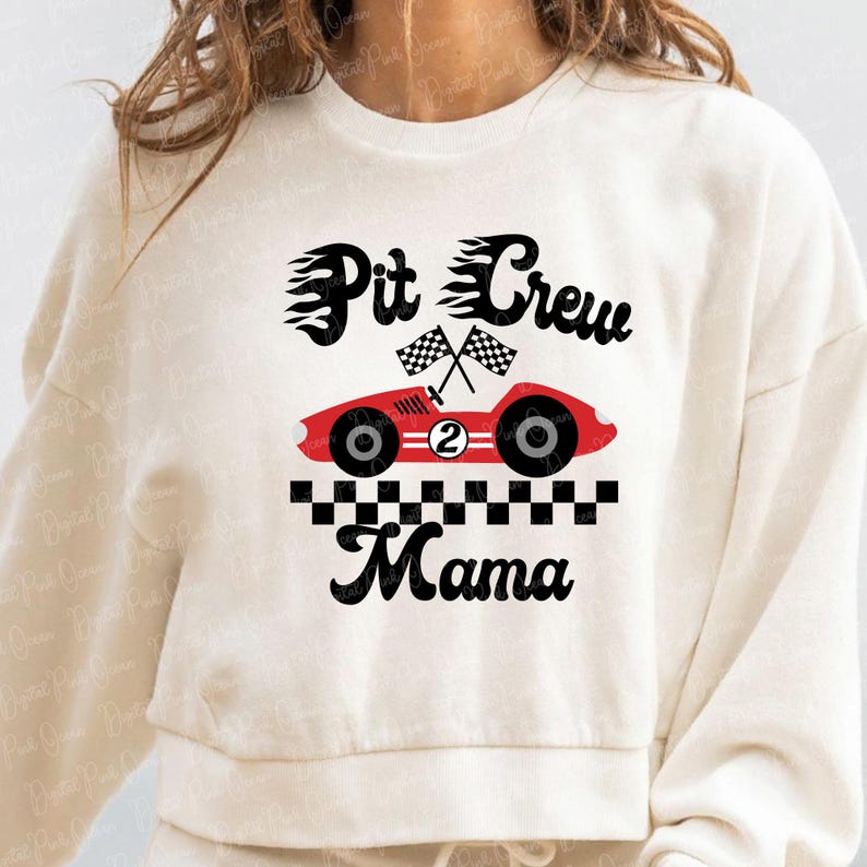 May include: Cream-colored sweatshirt with a red race car graphic, the number 2, and the words "Pit Crew Mama" in black. Two checkered flags are above the car. The design is centered on the front of the shirt.