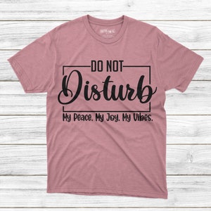 May include: A heather pink t-shirt with black text that reads "DO NOT Disturb My Peace. My Joy. My Vibes."