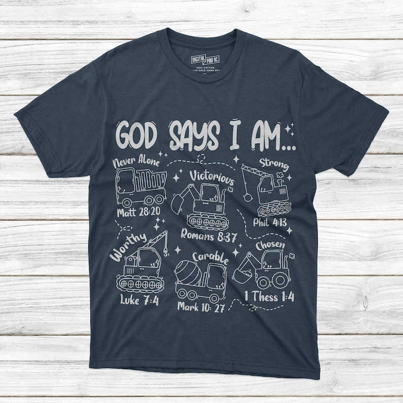 Puede incluir: Camiseta azul marino con texto blanco e ilustraciones de veh&iacute;culos de construcci&oacute;n. El texto dice "GOD SAYS I AM..." con frases como "Never Alone" y "Victorious" y vers&iacute;culos b&iacute;blicos. Un dise&ntilde;o &uacute;nico e inspirador.