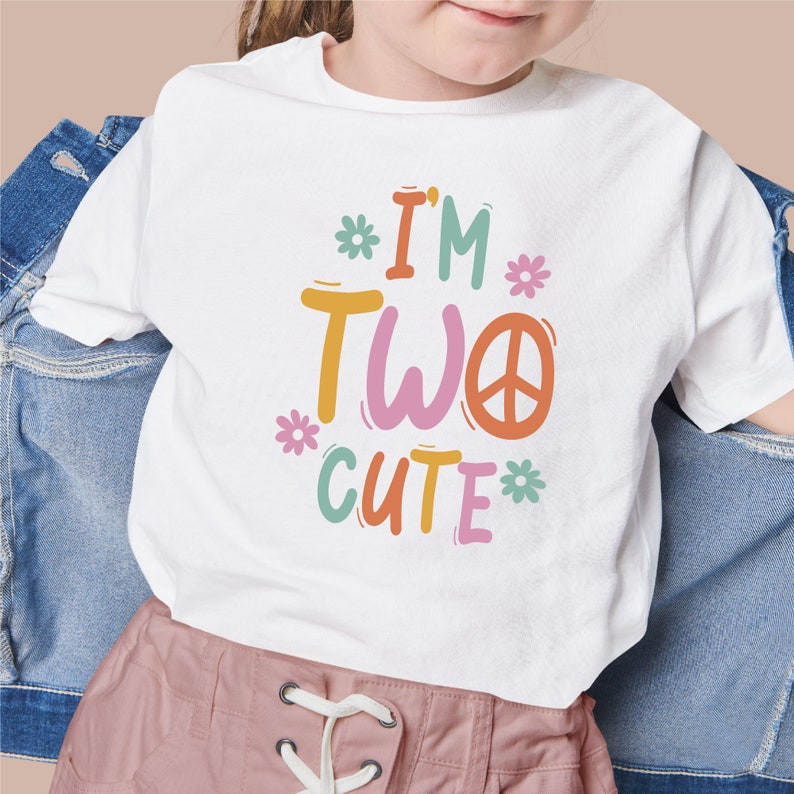 Puede incluir: Camiseta blanca con un gr&aacute;fico colorido que dice "I'm Two Cute" con un signo de paz y flores.