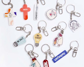 May include: Assortment of colorful keychains with religious and inspirational messages. Keychains feature images of a lightbulb, a salt shaker, a cross, a sheep, and a family. Some keychains have text such as "God Bless You", "Truth", "Be Light", "Be Salt", "Hallelujah", "Amen", and "Love Never Fails".
