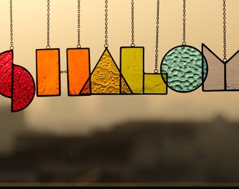 May include: A stained glass word art piece spelling out "SHALOM" in various colors and geometric shapes. The letters are suspended from chains.