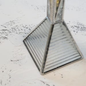 May include: A pyramid-shaped glass object with a square base and ribbed, clear glass panels held together by dark metal soldering. The structure tapers to a point at the top, featuring a reflective, geometric design with clean, straight lines.