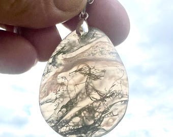 May include: A teardrop-shaped pendant with a silver chain. The pendant is made of a translucent stone with a natural, moss-like pattern in shades of green, brown, and white. The stone is held by a silver bail.
