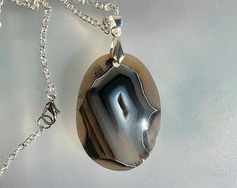 May include: A silver chain necklace with an oval pendant featuring a natural agate stone with brown, white, and black banding.