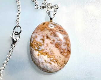May include: A silver chain necklace with a brown, white and pink agate pendant. The pendant is oval shaped and has a swirling pattern.