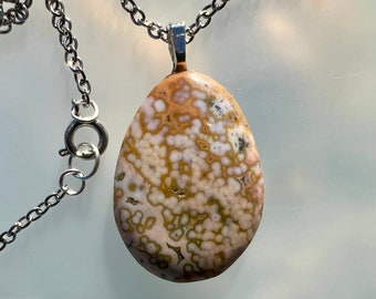 May include: A silver chain necklace with a pendant made of a light brown and white agate stone. The stone has a unique pattern of white and brown swirls.