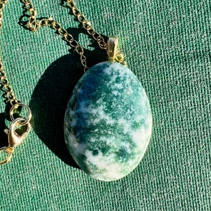 May include: A green and white agate stone pendant on a gold chain necklace. The stone is oval shaped and has a natural, organic look.