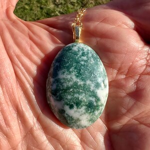 May include: A green and white agate pendant on a gold chain. The pendant is oval shaped and has a swirling pattern.