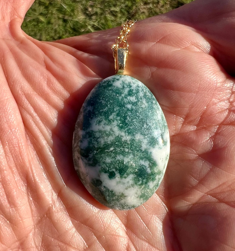 May include: A green and white agate pendant on a gold chain. The pendant is oval shaped and has a swirling pattern.