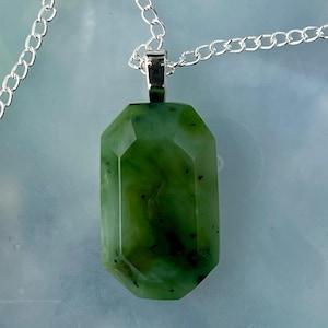 Könnte beinhalten: Eine silberne Kettenkette mit einem grünen Jade-Anhänger. Der Anhänger ist facettiert und hat eine rechteckige Form.