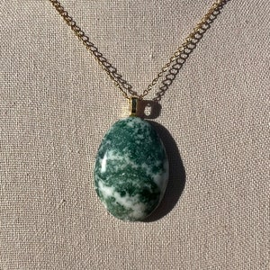 May include: A green and white agate stone pendant on a gold chain. The stone is oval shaped and has a marbled pattern.