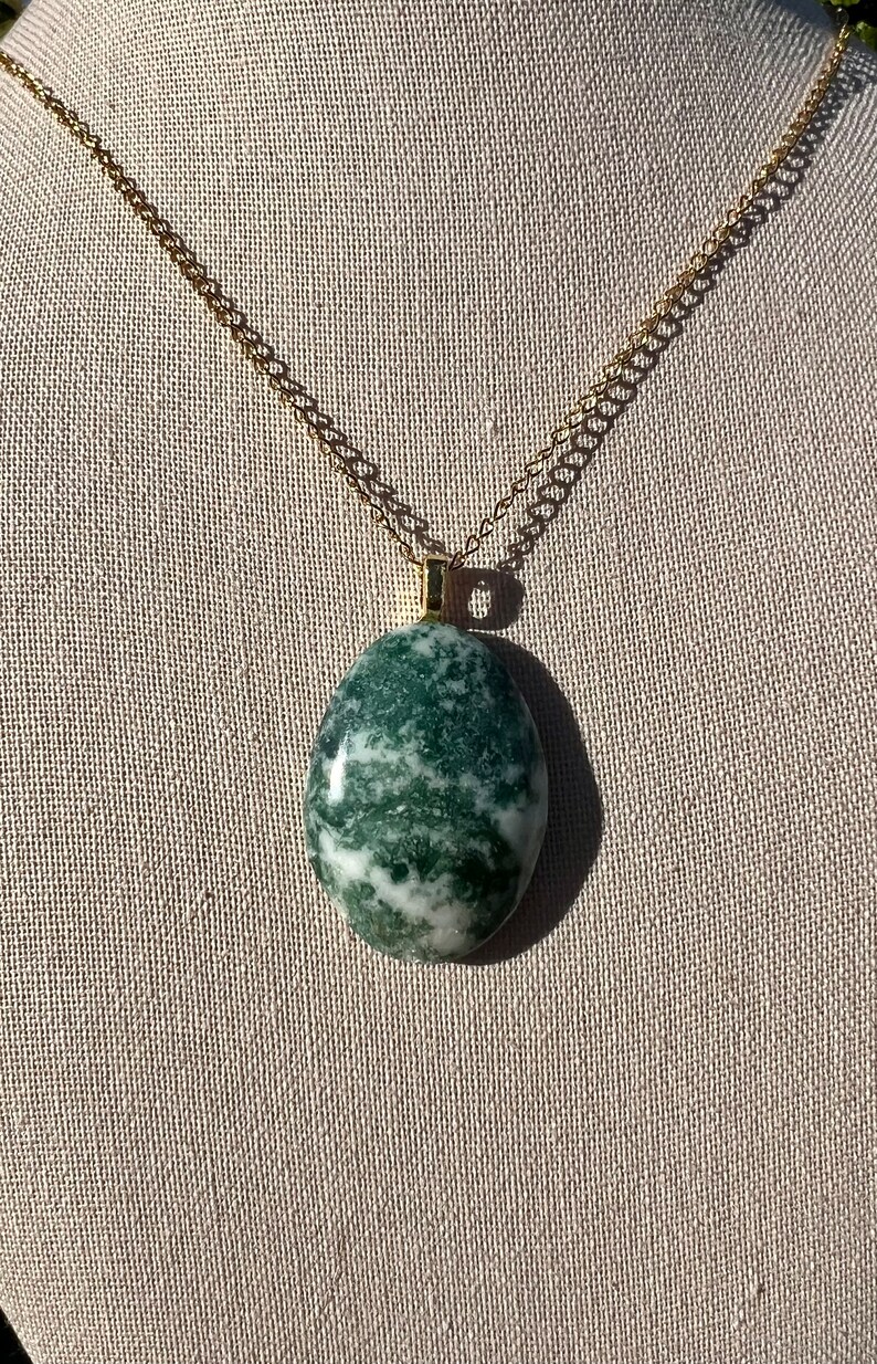 May include: A green and white agate stone pendant on a gold chain. The stone is oval shaped and has a marbled pattern.