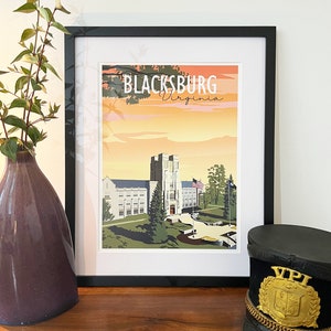 Pode incluir: Uma impressão emoldurada de uma ilustração de estilo vintage de um edifício com o texto "Blacksburg Virginia" no topo. O edifício é um edifício de tijolo branco com uma torre e um relógio. O edifício é cercado por árvores e grama. A impressão está em uma moldura preta.