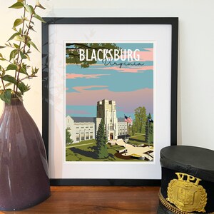 Pode incluir: Uma impressão emoldurada de uma ilustração de estilo vintage de um edifício com o texto "Blacksburg Virginia" acima. O edifício é de cor cinza claro com um telhado cinza escuro e uma torre alta. A ilustração está sobre um fundo de céu azul com nuvens cor-de-rosa.