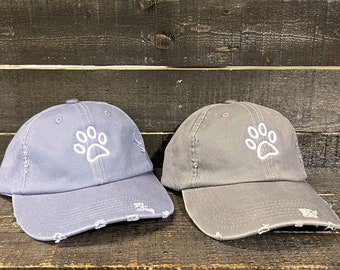 May include: Two gray distressed baseball caps with a white paw print embroidered on the front.