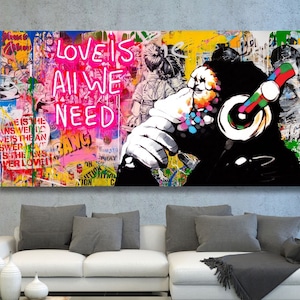 May include: A colourful abstract art print featuring a black and white image of a monkey wearing headphones. The background is a collage of colourful graffiti and text, including the words "Love is All We Need".