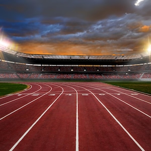 Könnte beinhalten: Eine leere Laufbahn in einem Stadion mit einer roten Oberfläche und weißen Linien. Das Stadion ist mit Zuschauern gefüllt und der Himmel ist bewölkt mit einem Sonnenuntergang im Hintergrund.