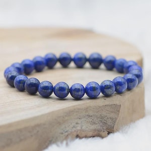 Op de afbeelding: Een blauwe kralenarmband. De armband is gemaakt van ronde, gepolijste kralen in een diepblauwe kleur. De kralen zijn aan elkaar geregen tot een complete cirkel. De armband ligt op een houten oppervlak.