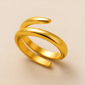 Peut inclure: Une bague dorée avec un design en spirale. La bague s'enroule autour du doigt avec une finition lisse et polie. La bague est faite d'un métal brillant et réfléchissant.