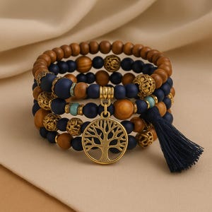 Könnte beinhalten: Gestapeltes Armband-Set mit Holzperlen, marineblauen matten Perlen und goldfarbenen Akzenten. Ein goldener Lebensbaum-Anhänger und eine marineblaue Quaste vervollständigen das Design. Die Armbänder sind gestapelt.