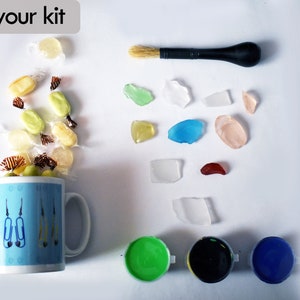 Puede incluir: Un kit de manualidades con una taza azul llena de caramelos, un pincel, vidrio de mar de varios colores y tres peque&ntilde;os botes de pintura en verde, negro y azul.
