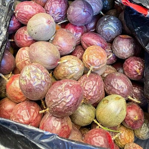 Puede incluir: Primer plano de una gran bolsa de pl&aacute;stico llena de fruta de la pasi&oacute;n. La fruta es una mezcla de p&uacute;rpura, verde y marr&oacute;n, y algunas de las frutas se han cortado para revelar las semillas en el interior.