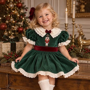 May include: A dark green velvet dress featuring a white lace-trimmed collar, a small burgundy bow at the neckline, and a matching burgundy velvet waistband. The dress includes a nutcracker embroidery on the bodice and white lace trim on the sleeves.