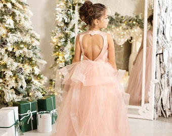 Peut inclure: Une jeune fille portant une robe en tulle rose avec une découpe en forme de cœur dans le dos. Elle se tient devant un sapin de Noël et un miroir.