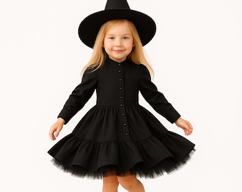 Puede incluir: Un disfraz de bruja negro para niña, que incluye un vestido de manga larga con botones y una falda escalonada. El conjunto incluye un sombrero de bruja negro a juego. La falda tiene un dobladillo de tul.
