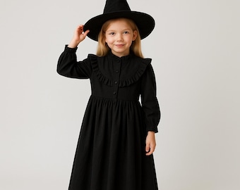 May include: A young person wearing a black witch costume, including a long-sleeved dress with a ruffled collar and a pointed hat. The dress has buttons down the front and a flared skirt. The hat is black and has a wide brim.