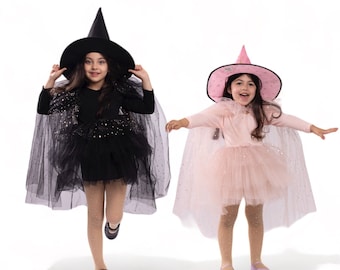 Puede incluir: Dos chicas vestidas con disfraces de Halloween. Una chica lleva un disfraz de bruja negro con un sombrero negro y una capa de tul negro. La otra chica lleva un disfraz de princesa rosa con un sombrero rosa y una capa de tul rosa.