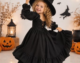 May include: A black long-sleeved dress with a ruffled hem and a lace-up back detail, paired with a matching black pointed witch hat. The dress features a square neckline and puffed sleeves, creating a full skirt silhouette for a costume ensemble.