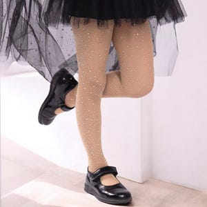 K&ouml;nnte beinhalten: Eine nude farbene Netzstrumpfhose mit kleinen wei&szlig;en Strasssteinen. Die Strumpfhose wird von einer Person getragen, die schwarze Schuhe und einen schwarzen T&uuml;llrock tr&auml;gt.